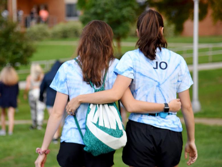 Two Orientation Leaders leave an orientation event arm in arm